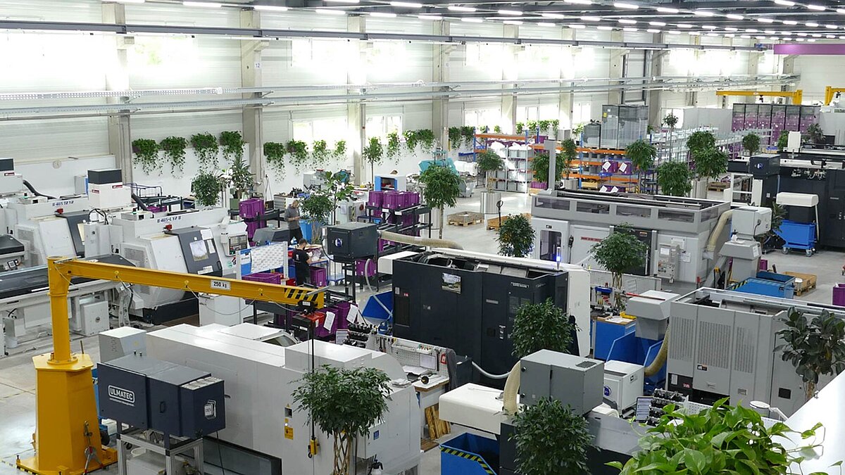 Produktionshalle; In der Produktionshalle gibt es verschiedene Maschinen und einige Pflanzen. Die Menschen arbeiten an ihren Arbeitsplätzen. 