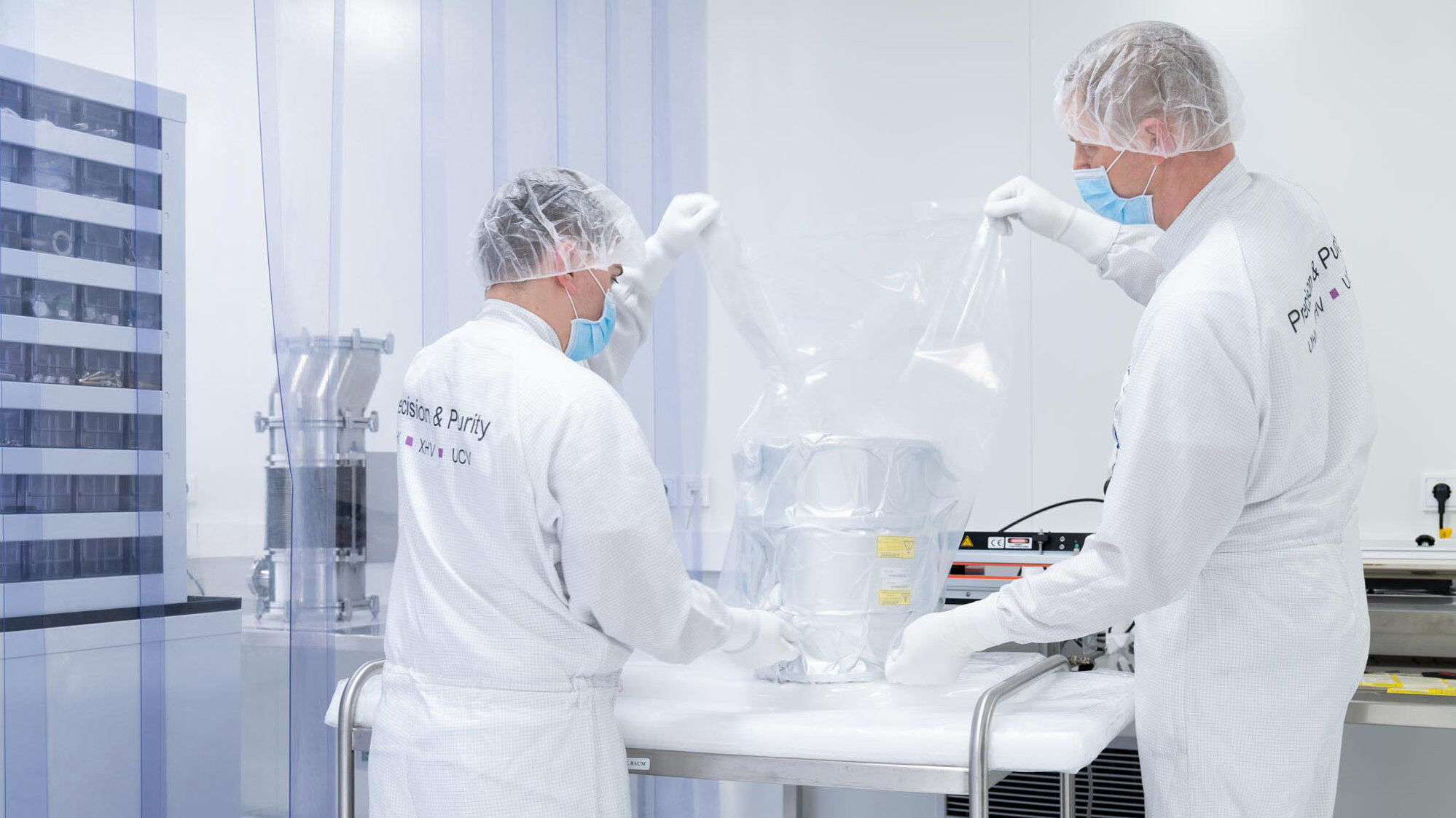 Two employees pack components under cleanroom conditions