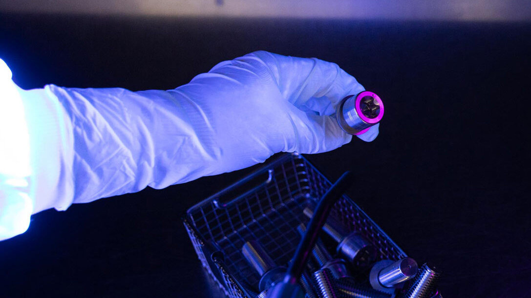 Durchlässigkeitsbestimmung; Ein Mitarbeiter prüft mit einer Schwarzlichtlampe, ob sich auf einem der Produkte eine Verunreinigung befindet