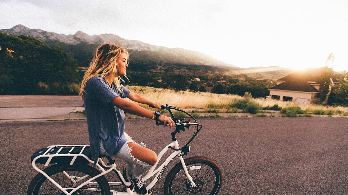 https://en.freejpg.com.ar/free/info/100023929/girl-woman-bike-bicycle-blonde-people-lifestyle Businessbike Vorteile; Eine junge Frau fährt mit ihrem E-Bike auf einer Straße